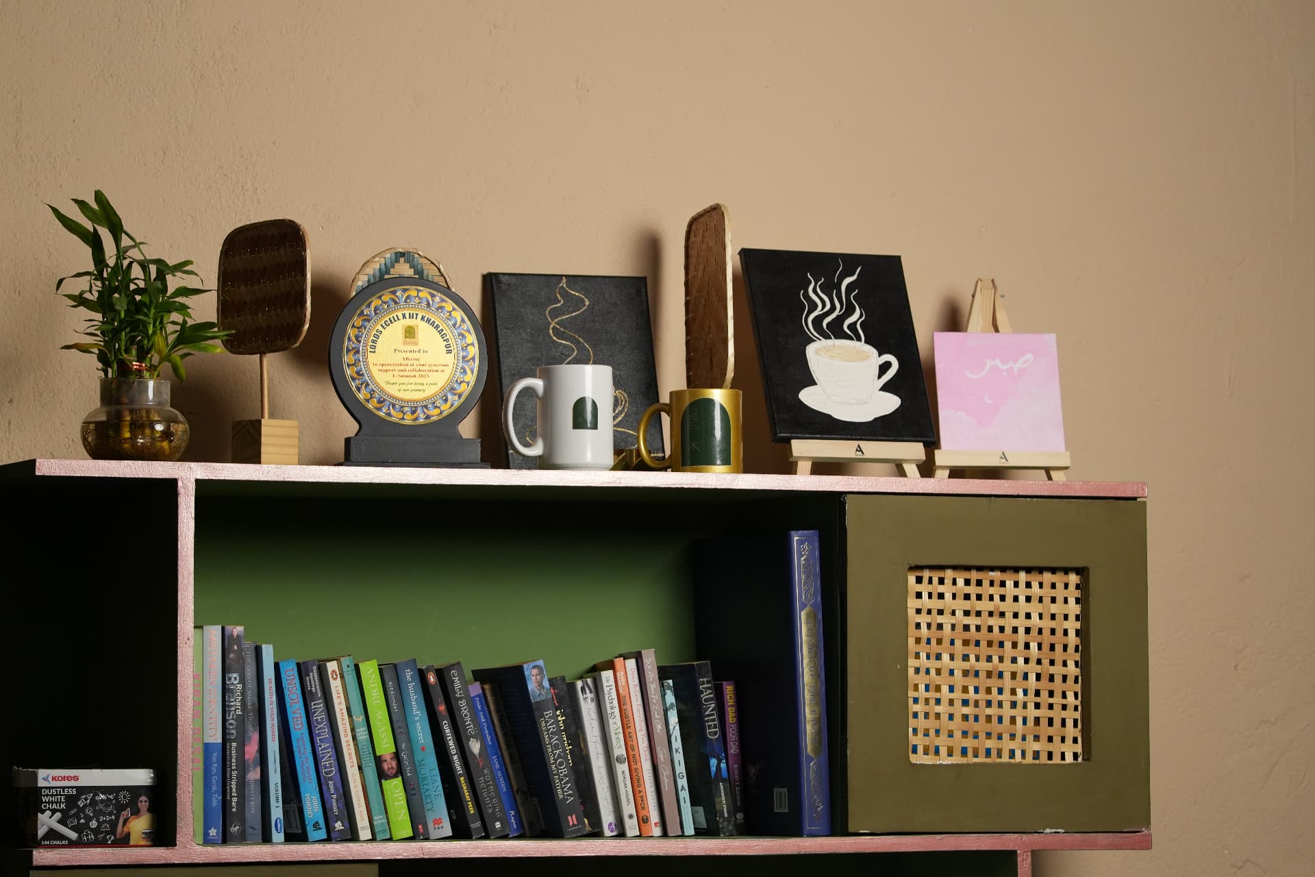 Bookshelf at Alkemy with plants, mugs and hand-painted canvases